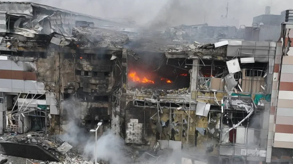 A multi-story commercial building in Kyiv heavily damaged by a missile strike, with fire visible inside the gutted structure and smoke rising from the rubble