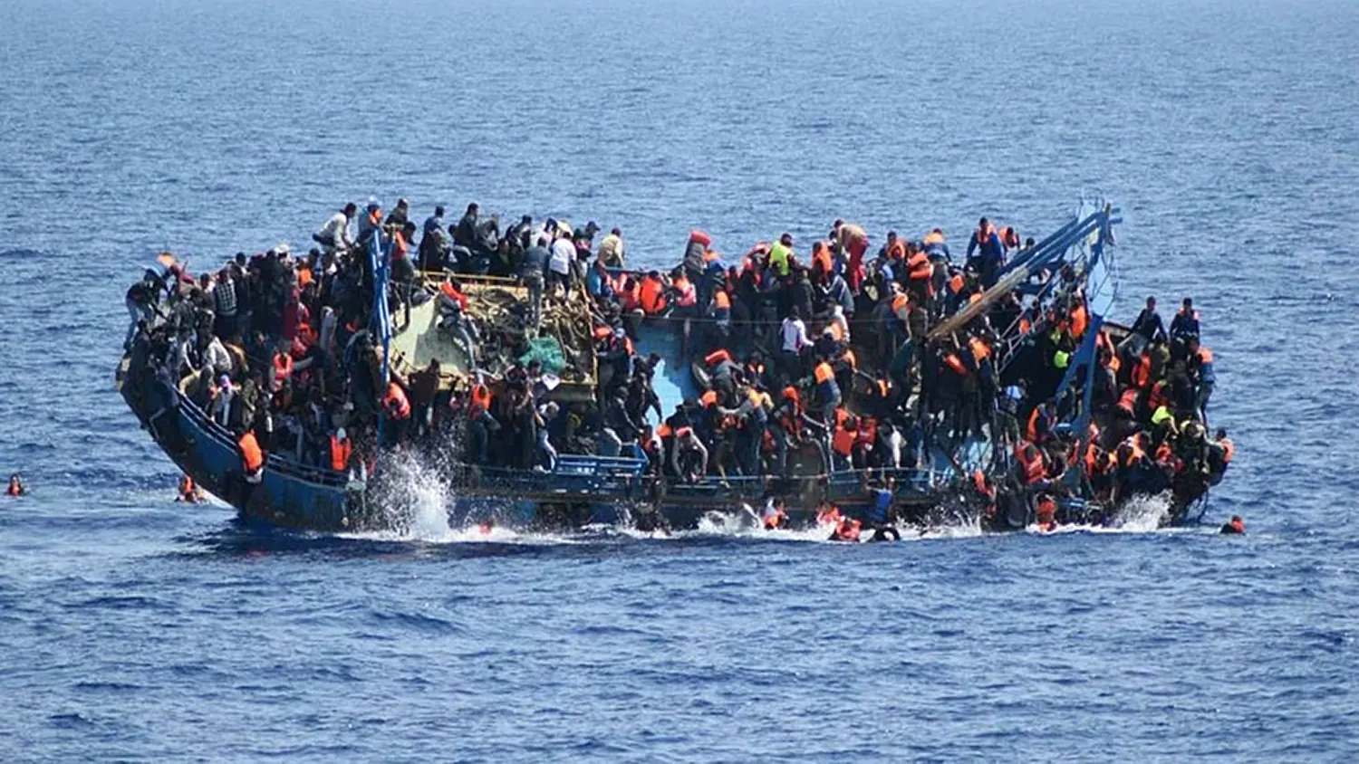A crowded blue wooden boat packed with hundreds of African migrants listing and capsizing in the open sea off the coast of Yemen