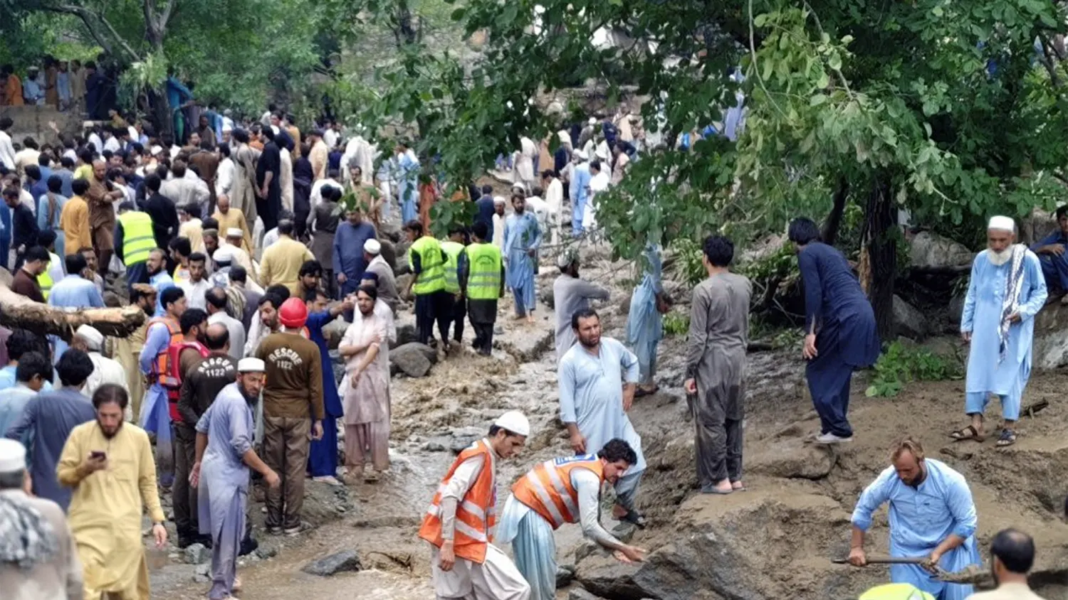 Emergency rescue workers and local volunteers helping stranded residents and tourists navigate a debris-filled stream following a deadly flash flood in Northern Pakistan, 2025.