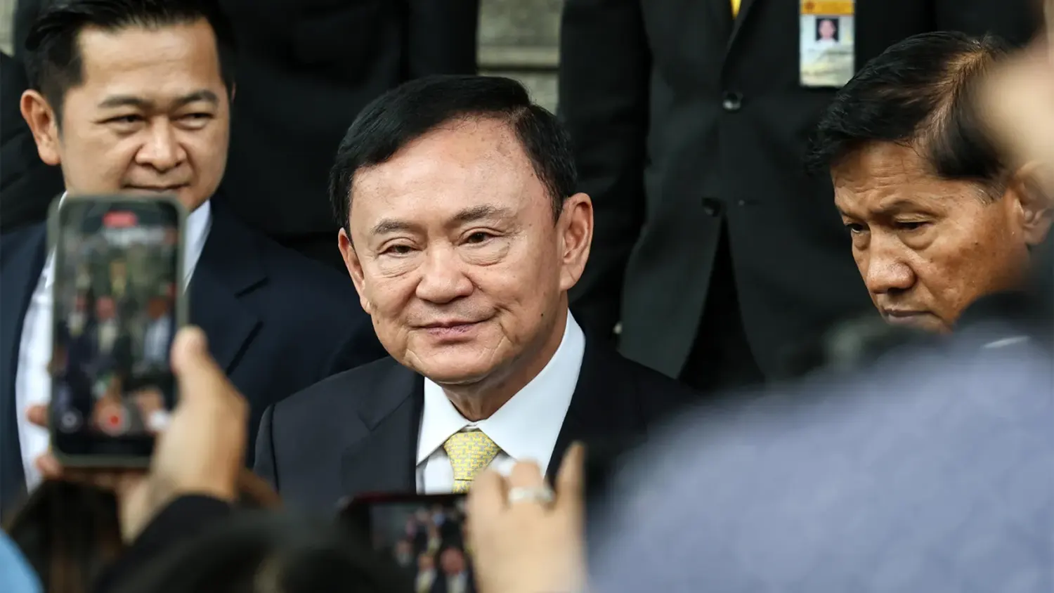 Former Thai Prime Minister Thaksin Shinawatra smiling while surrounded by security and reporters, following his acquittal of royal defamation charges in Bangkok.