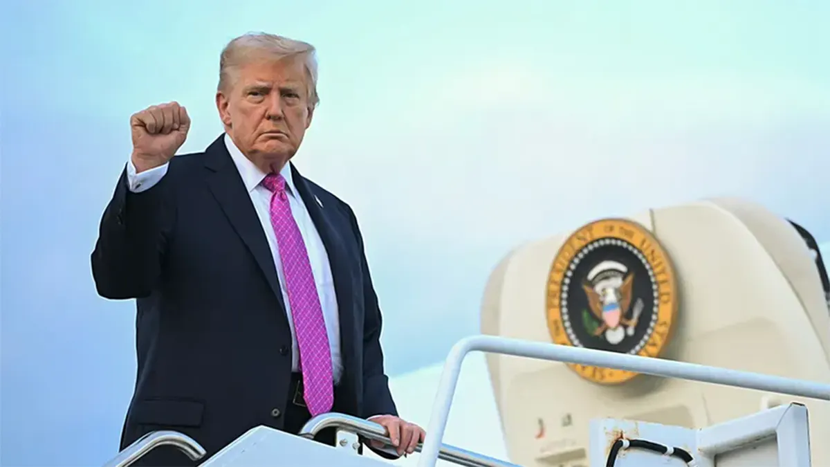President Donald Trump standing on the steps of Air Force One, raising his right fist, with the Presidential seal visible on the aircraft door behind him.