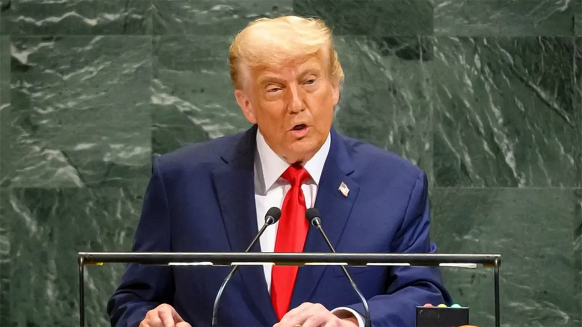 Donald Trump speaking from a wooden podium with two microphones during a speech at the United Nations General Assembly, set against the iconic green marble wall backdrop