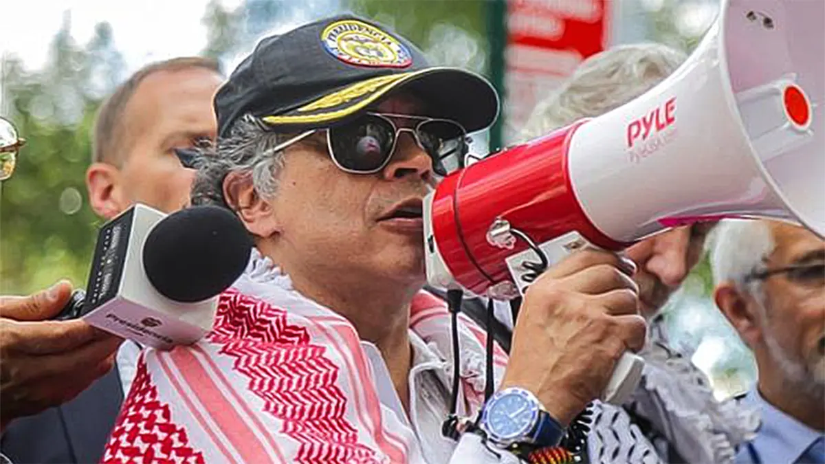 Colombian President Gustavo Petro wearing a black cap and sunglasses, draped in a red and white keffiyeh scarf, speaking forcefully into a white and red Pyle megaphone amidst a crowd.