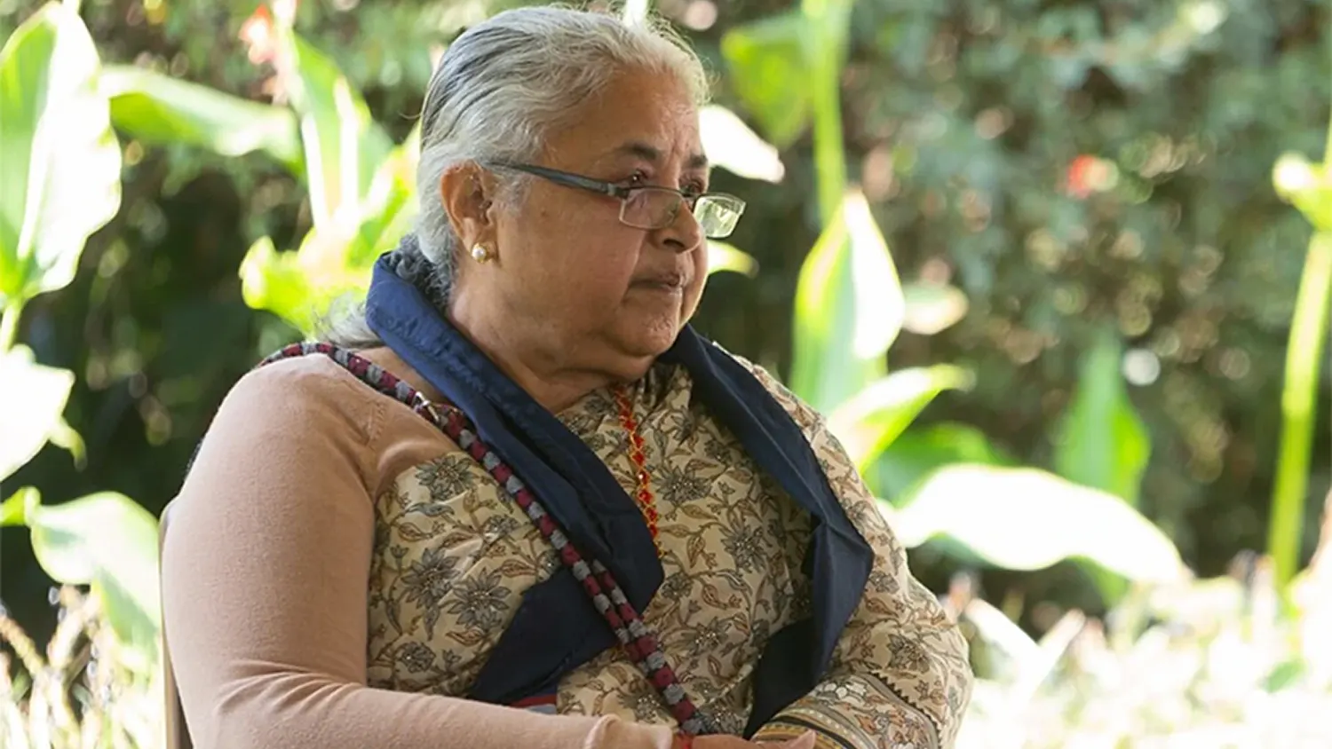 Profile portrait of Sushila Karki, Nepal's first female Prime Minister and former Chief Justice, seated outdoors in a garden setting