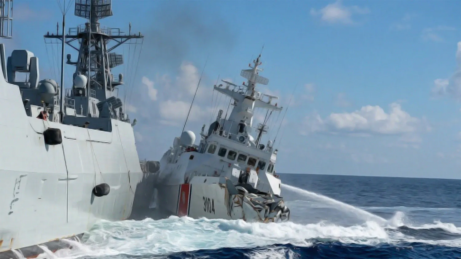 Dramatic close-up of a maritime collision in the South China Sea where a China Coast Guard ship collides with a gray naval warship amid splashing white water.