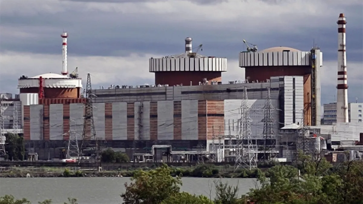 An exterior, wide panoramic shot of the South Ukraine Nuclear Power Plant showing its massive reactor units, containment structures, and electrical grid infrastructure under a cloudy sky.