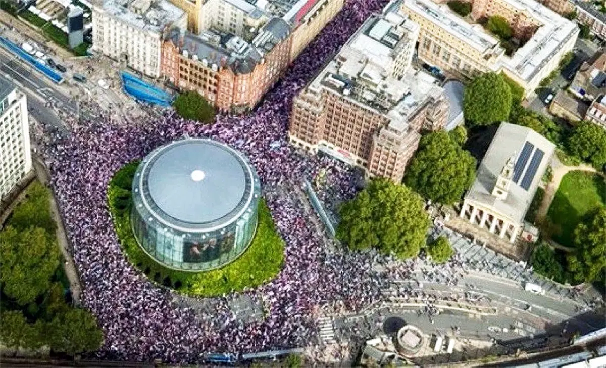 An overhead aerial view of thousands of protesters wearing purple and white filling the streets around the BFI IMAX roundabout in Waterloo, London, during the Unite the Kingdom rally in September 2025.