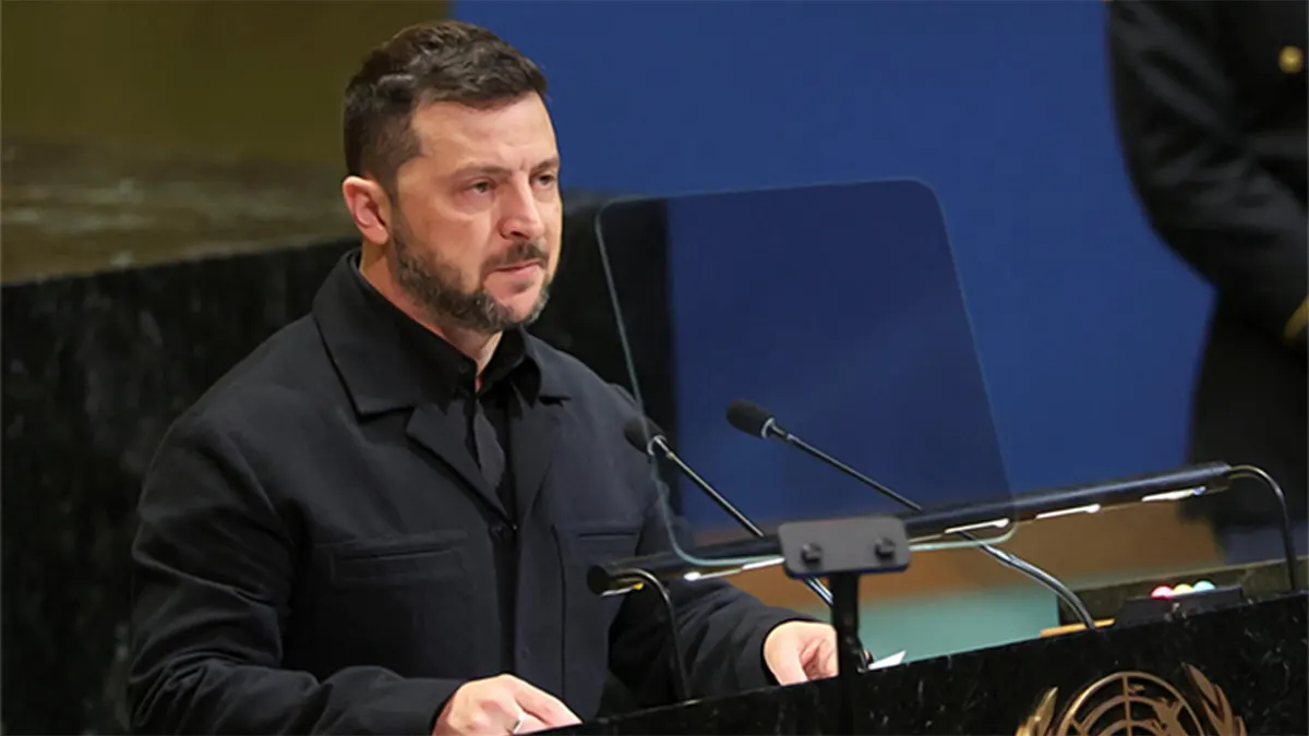 Ukrainian President Volodymyr Zelenskyy wearing a black buttoned jacket, standing behind a dark marble podium with two microphones during a speech at the United Nations General Assembly hall.