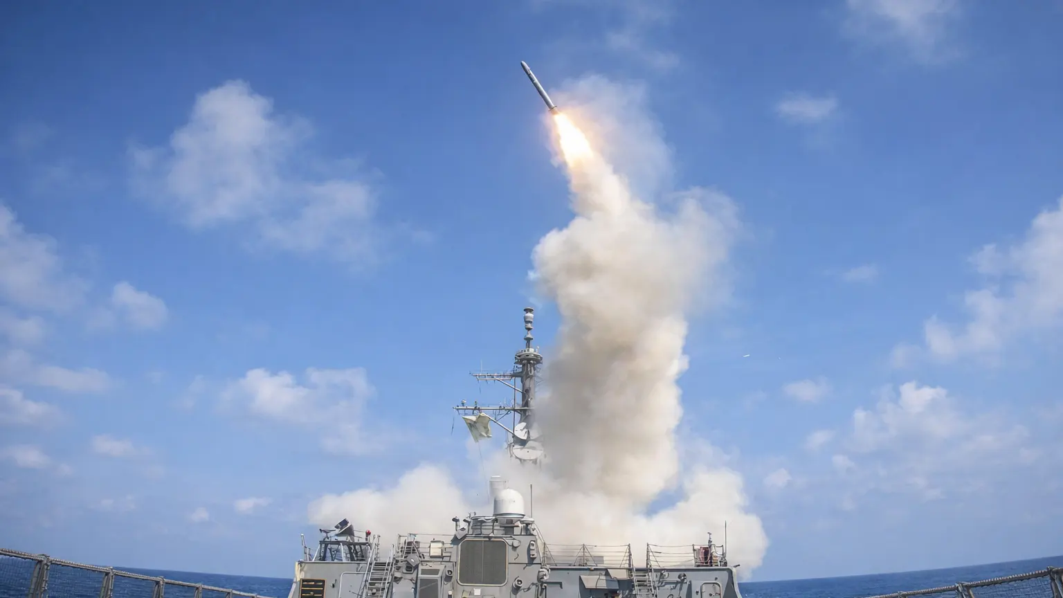 U.S. Navy destroyer launching a missile during military operations in the Strait of Hormuz, with smoke rising over the Persian Gulf