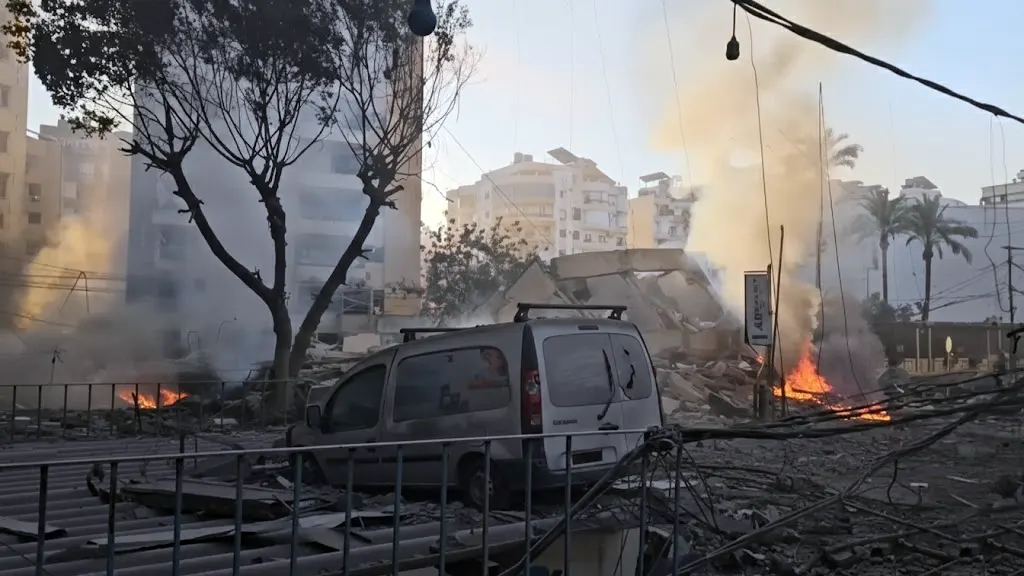 Destroyed silver van and burning debris in a rubble-strewn street in southern Lebanon following 2026 Israeli airstrikes