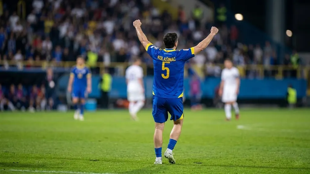 Bosnia and Herzegovina defender Sead Kolašinac (number 5) celebrates with arms raised in a packed stadium after defeating Italy in the 2026 World Cup Play-off final. High-resolution sports photography with cinematic bokeh