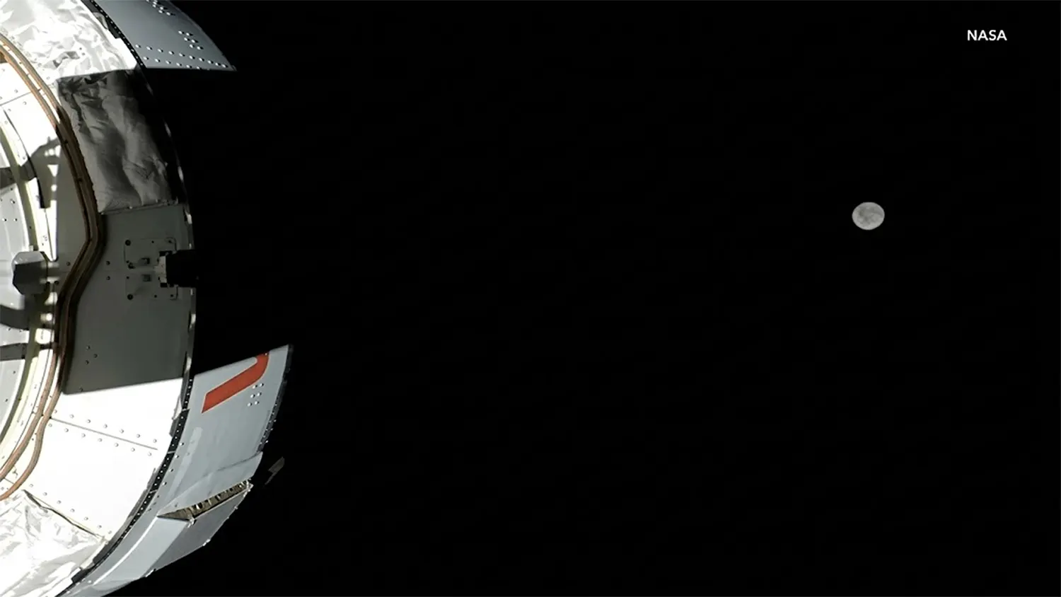 A high-resolution view from the NASA Artemis II Orion spacecraft showing the curved hull of the capsule in the foreground and the distant, cratered Far Side of the Moon against the black void of space