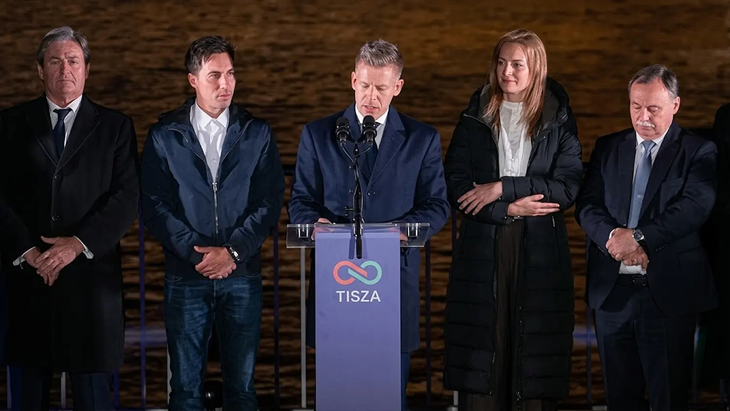 Péter Magyar delivering his victory speech at a Tisza Party podium following the 2026 Hungarian general election, flanked by party members at night