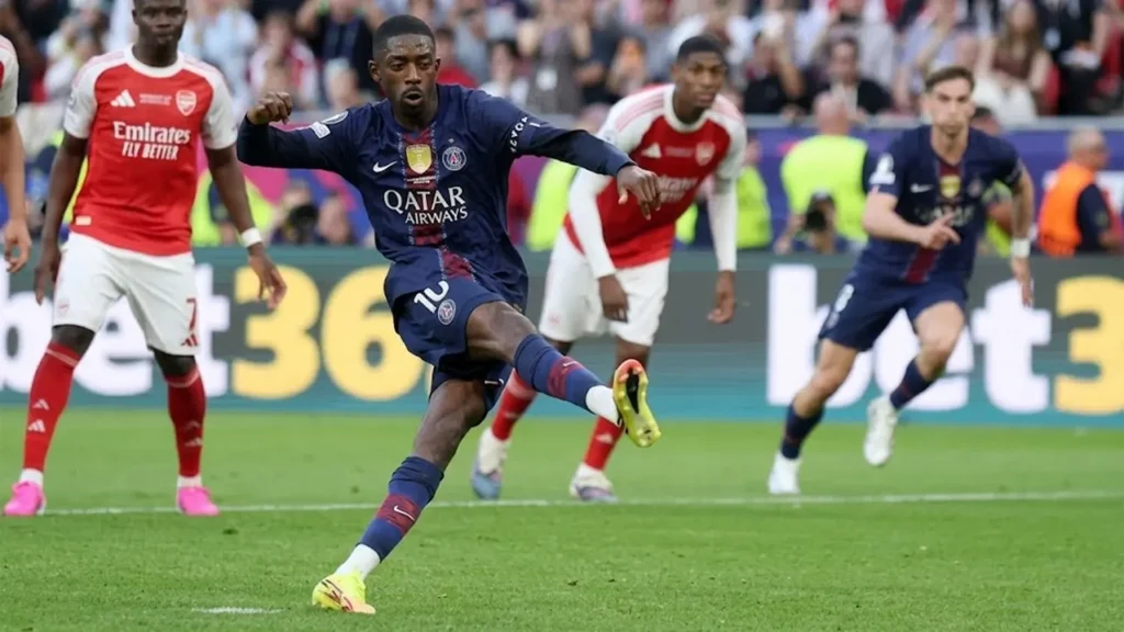 PSG winger Ousmane Dembélé taking a powerful shot with his left foot while surrounded by Arsenal defenders during a UEFA Champions League match.