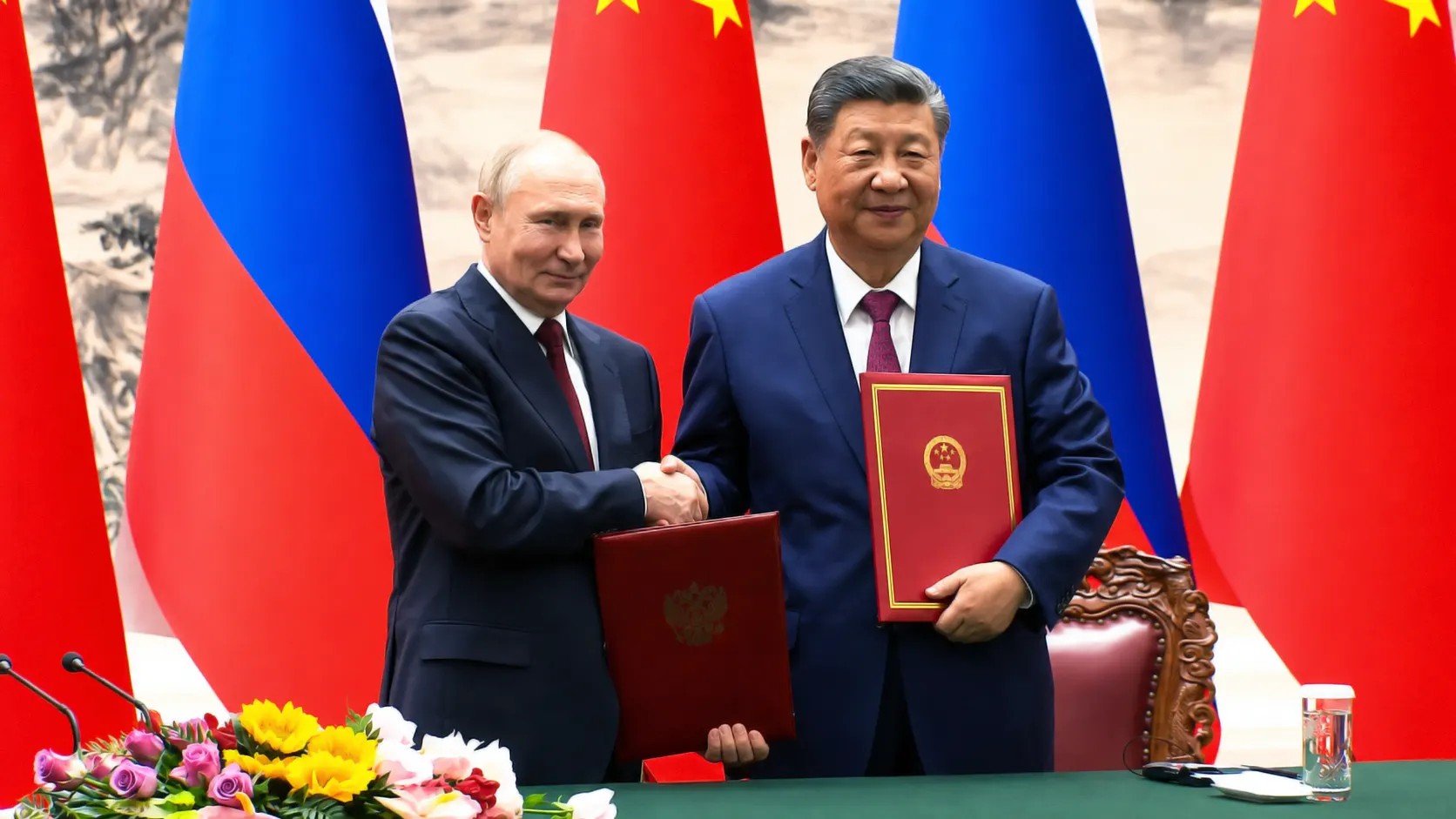 Russian President Vladimir Putin and Chinese President Xi Jinping shaking hands and holding official signed treaty folders during a bilateral summit, set against Russian and Chinese flags