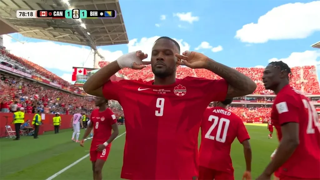 Canada striker Cyle Larin celebrating his equalizing goal against Bosnia and Herzegovina with fingers in ears at Toronto Stadium during the 2026 FIFA World Cup.
