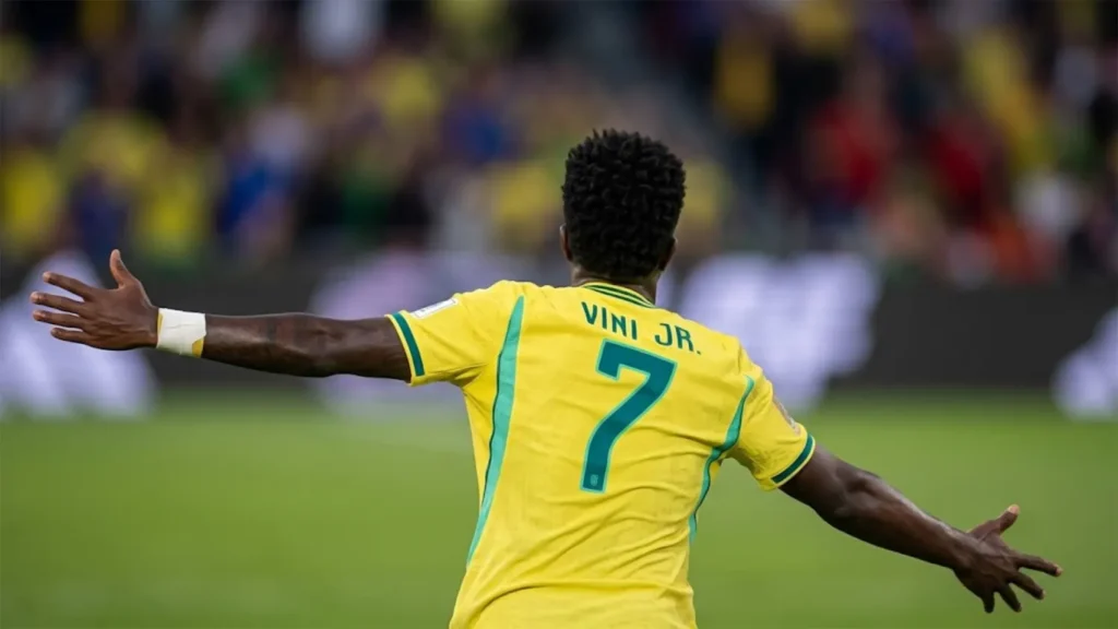 Rear view of Vinicius Jr. wearing the number 7 yellow Brazil jersey with arms outstretched celebrating his goal against Morocco at the 2026 World Cup.