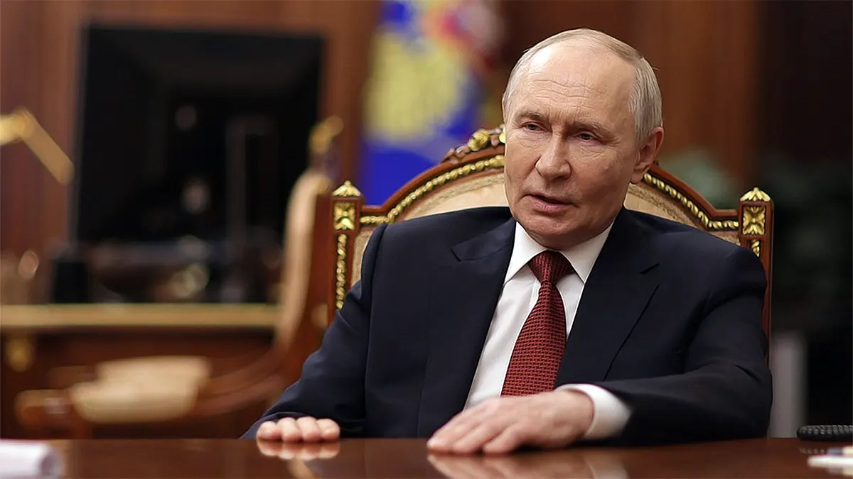 Russian President Vladimir Putin in a dark suit and red tie, seated at a wooden desk in front of the Russian Federation flag during an official address.