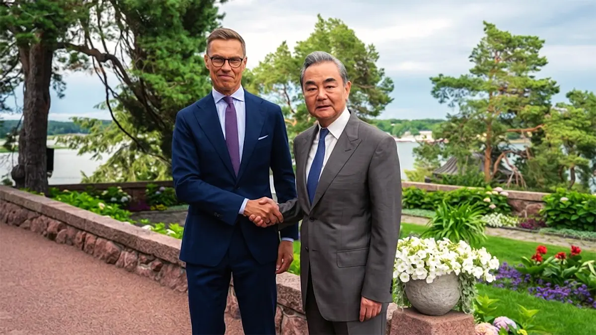 A high-resolution photograph capturing Finnish President Alexander Stubb (left) and Chinese Foreign Minister Wang Yi (right) shaking hands firmly in an outdoor garden setting in Turku, Finland, against a backdrop of a river and pine trees.