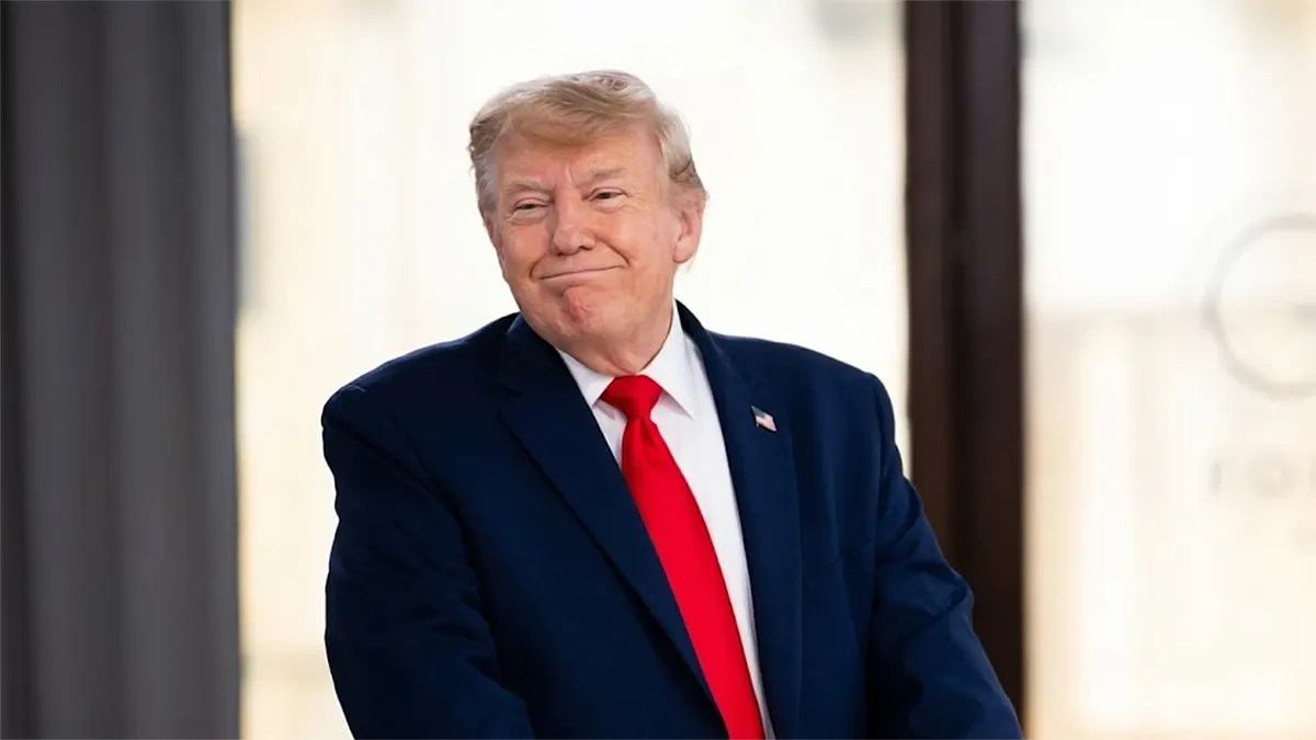 A high-resolution, sharp portrait of Donald Trump smiling slightly, wearing a navy blue suit, a vibrant red tie, and a US flag lapel pin against a blurred background.