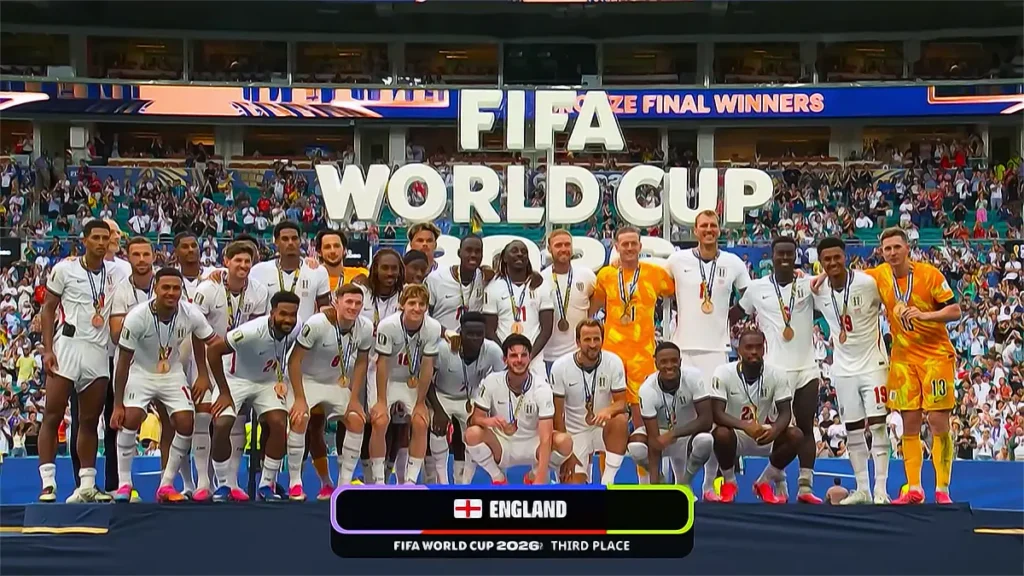 The England national football team squad poses on a presentation stage for a group photo wearing medals after winning third place at the FIFA World Cup 2026, with a large 'FIFA WORLD CUP 3RD PLACE' sign in the background.