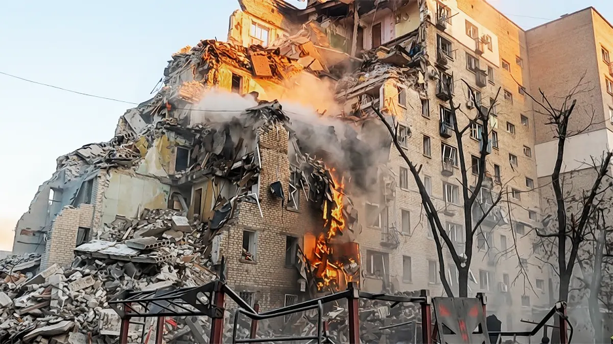 A multi-story residential apartment building in Kyiv severely damaged and partially collapsed with active fires and smoke following a missile strike.