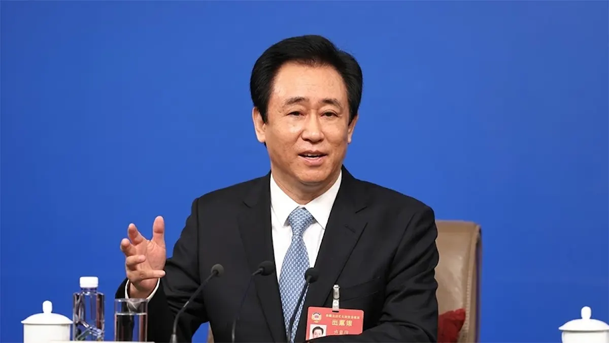 Evergrande founder Hui Ka Yan speaking at a press conference microphone setup in front of a blue background.