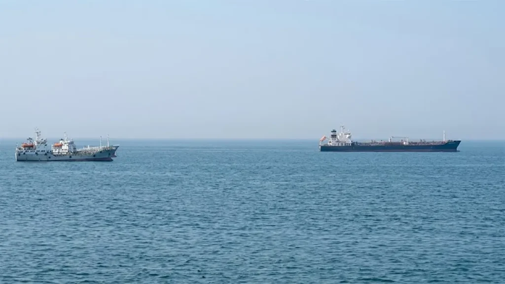Two large cargo ships and oil tankers navigating open blue waters during a maritime standoff in the Strait of Hormuz.