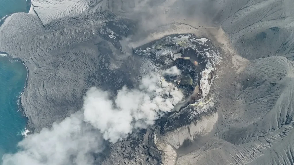 High-angle aerial drone image showing the smoking crater caldera and ash emissions of Mount Anak Krakatau volcano in the Sunda Strait.