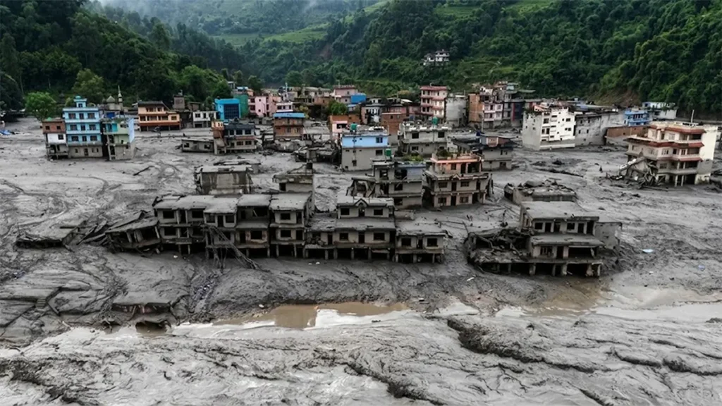 Aerial drone view of flood damage showing multi-story buildings partially submerged in thick grey mud and silt after a major flash flood in Nepal.